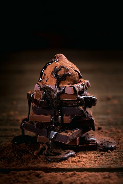 شربت شکلات که روی پشته شکلات تیره و شیر شکل گرفته ترافل است شکلات با پودر کاکائو روی میز چوبی روستایی تیره شیرینی و پس زمینه شکلات