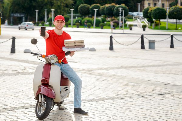 مرد تحویل تلفن و جعبه همراه با پیتزا سفارش آنلاین از وب سایت غذا برای مهمانی
