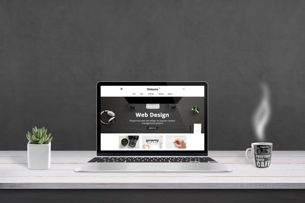 ارائه آژانس طراحی وب با طراحی سایت صاف و پاسخگو بر روی صفحه نمایش لپ تاپ فنجان قهوه و بشقاب کنار دیوار سیاه در پس زمینه