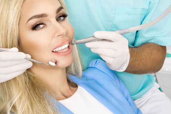 زن زیبا و جوان با دندانهای سفید زیبا که روی صندلی دندانپزشکی نشسته است دندانپزشک دندان های خود را درمان می کند