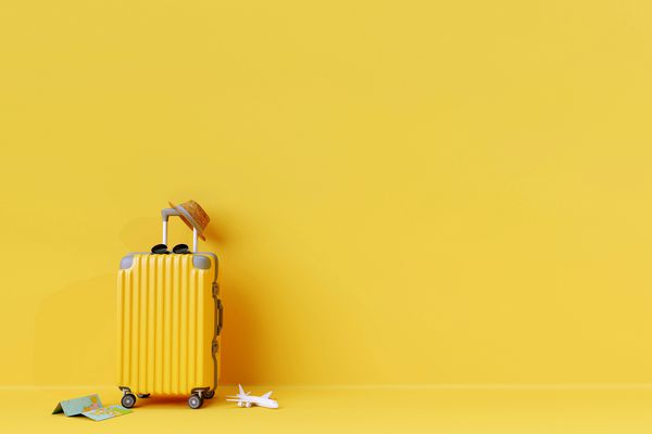 چمدان زرد با عینک آفتاب و کلاه با زمینه زرد مفهوم سفر سبک حداقل