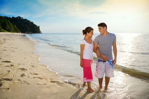 زوج خوشبختی که در امتداد یک ساحل غروب خورشید عاشقانه قدم می زنند