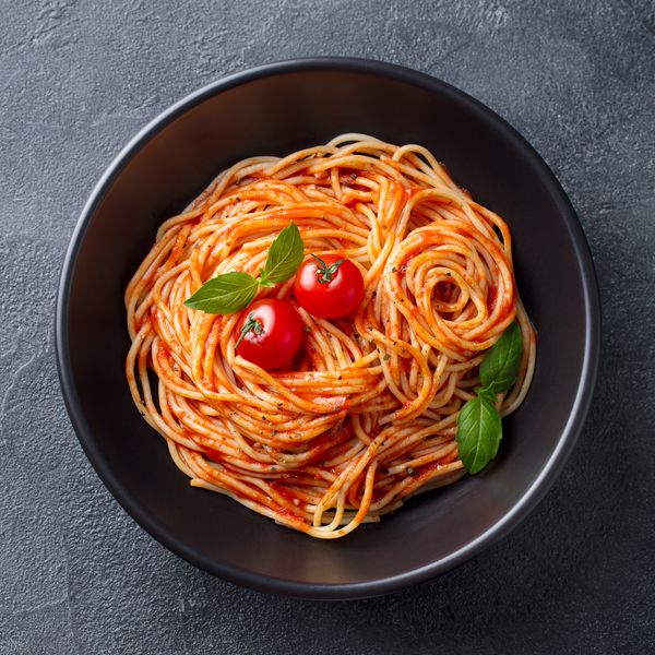 ماکارونی اسپاگتی با سس گوجه فرنگی در کاسه سیاه زمینه سنگ خاکستری نمای بالا نزدیک