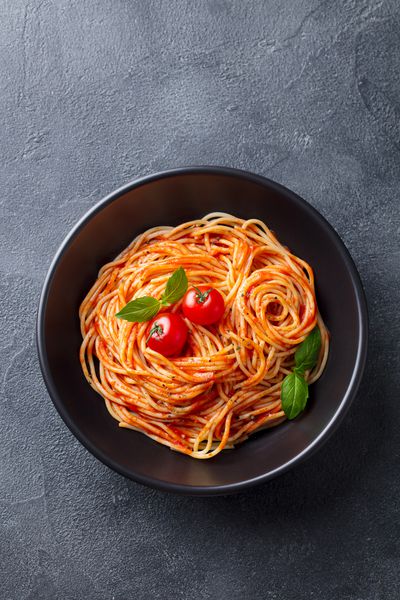 ماکارونی اسپاگتی با سس گوجه فرنگی در کاسه سیاه و در زمینه سنگ خاکستری نمای بالا