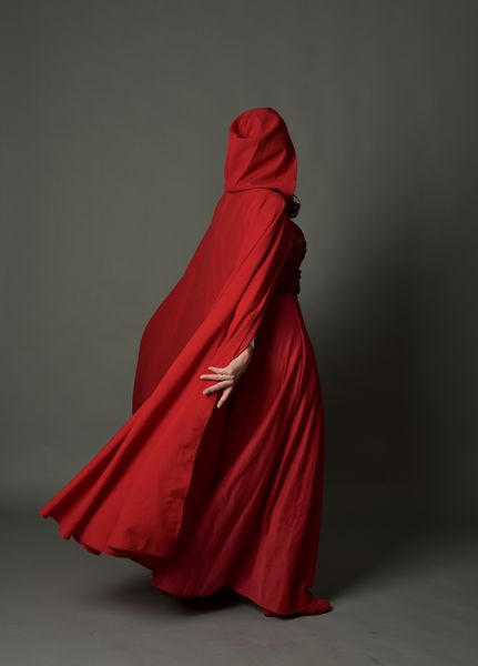 پرتره با طول کامل دختری که لباس مجلسی فانتزی قرمز با لباس عبا دارد ایستاده در پس زمینه استودیوی پسر
