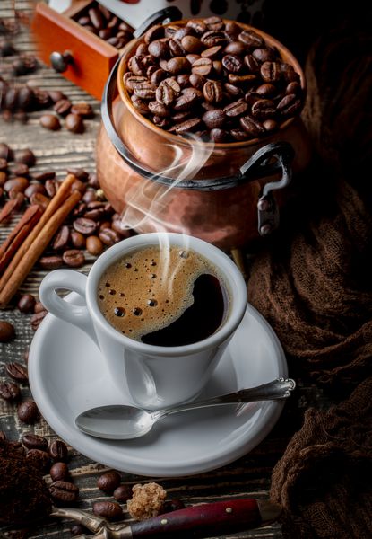 قهوه سیاه را در یک فنجان بر روی زمینه دانه های قهوه در ترکیب با لوازم جانبی