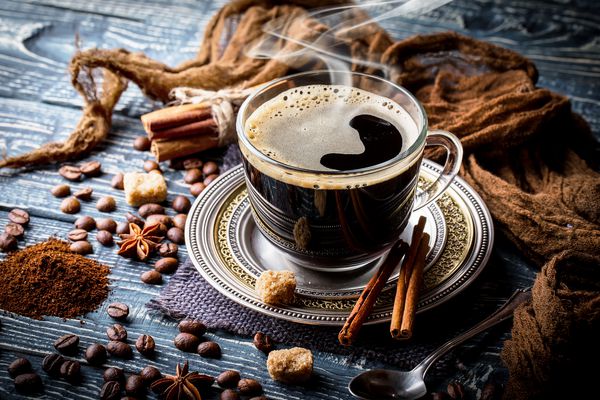 قهوه سیاه را در یک فنجان بر روی زمینه دانه های قهوه در ترکیب با لوازم جانبی