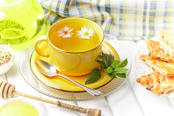 چای سبز را در یک فنجان روی یک پس زمینه برگهای خشک چای گل به صورت ترکیبی با لوازم جانبی در یک زمینه سفید