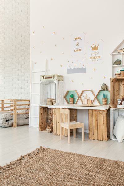 صندلی چوبی کوچک در کنار میز و قفسه های جعبه ای در فضای داخلی اتاق کودک کودک Scandi سفید با فرش و پوسترهای روی دیوار