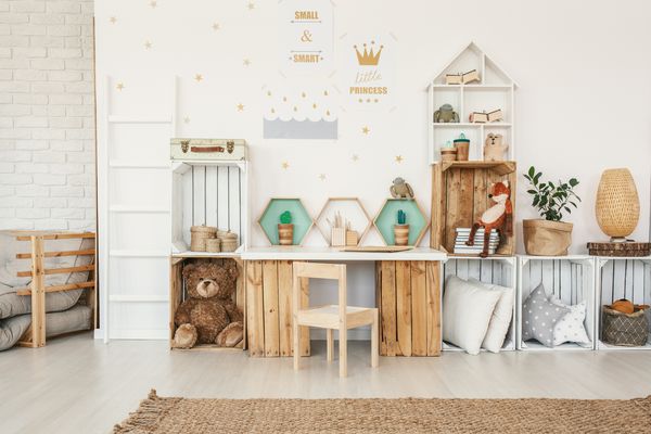 فضای داخلی اتاق کودک سفید با پوسترهای طلا روی دیوار اسباب بازی ها و بالش هایی که روی قفسه های جعبه و میز با کاکتوس های مصنوعی قرار داده شده