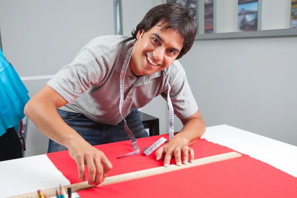 پرتره پیراهن دار مرد جوان اندازه گیری پارچه قرمز با خط کش روی میز