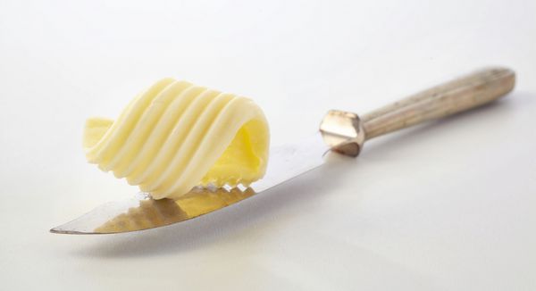 پیچ و تاب پیچیده مزرعه کره تازه زرد رنگ نمایش داده شده بر روی چاقوی کره نقره ای پرنعمت به طور مورب از طریق قاب با فضای کپی در یک ظاهر طراحی مواد غذایی یا ارائه مفهوم