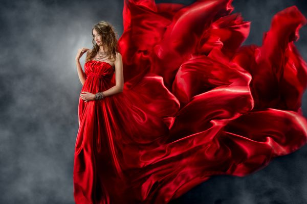 زن با لباس ابریشمی قرمز که از باد می وزد پارچه لباس راحتی و پرواز را بر روی زمینه خاکستری بپوشانید