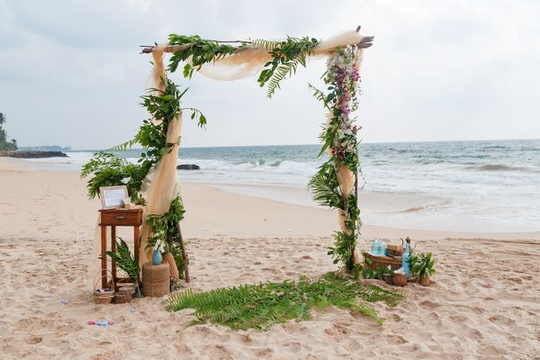 محل عروسی ساحل عروسی در ساحل قوس عروسی که از مواد و گلها در ساحل شن گرمسیری تزئین شده است مفهوم عروسی و ماه عسل