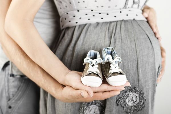 چکمه های نوزاد تازه متولد شده در دست والدین شکم زن باردار