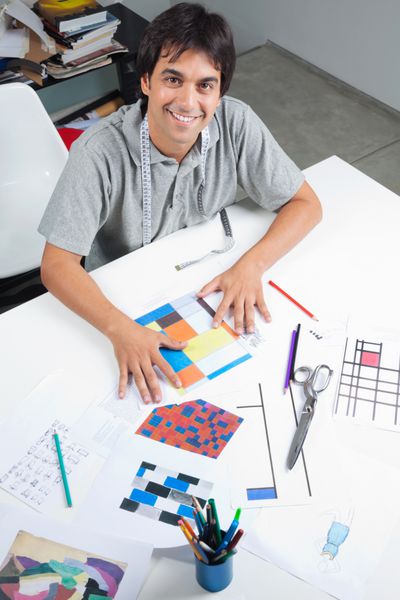 نمای زاویه ای بالا از طراح مد مرد که در جدول قرار دارد با طرح ها و الگوهای کلی در کارگاه