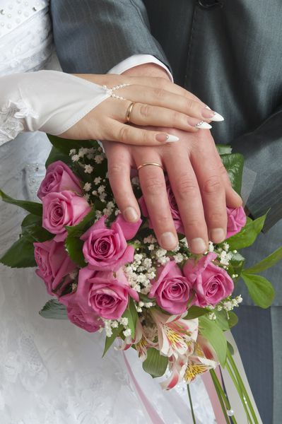 یک زن و شوهر تازه عروس دست خود را روی دسته عروسی قرار می دهند که باندهای عروسی خود را نشان می دهد