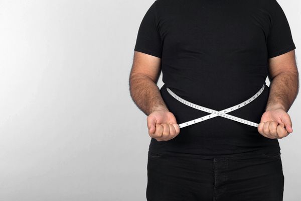 ضربات كلوز مرد چاق نوار اندازه گيري را در اطراف ضربات قرار مي دهد و وزن او را بر روي زمينه خاکستري اندازه مي گيرد