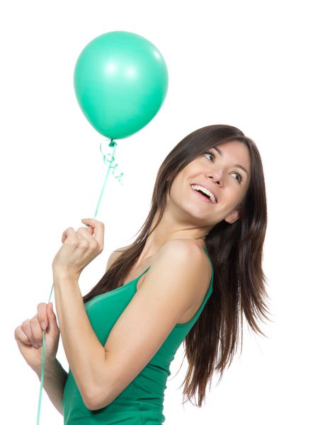 دختر جوان با بادکنک سبز به عنوان هدیه ای برای جشن تولد که در یک زمینه سفید لبخند می زند