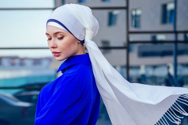 حجاب زن تجارت مسلمان مسلمان با آرایش ایستاده در خیابان در پس زمینه آسمان خراش ها این زن در لباس نیکای آبیای شیک پوشیده است