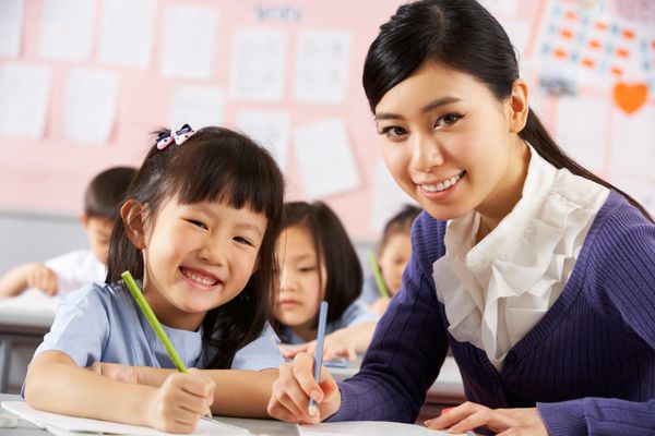 معلم کمک می کند تا دانش آموزان شاغل در میز در کلاس درس مدرسه چینی