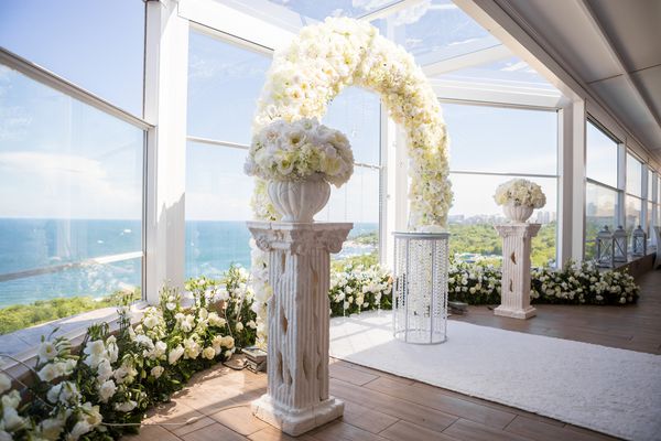 مراسم عروسی داخلی با قوس عروسی سفید که با گلها و کریستال های سفید تزئین شده است
