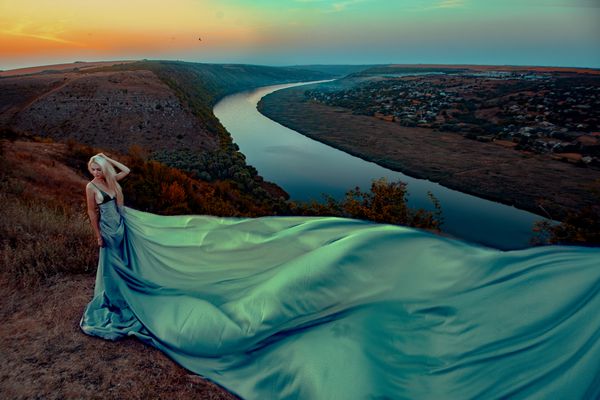 زن زیبا با لباس بلند در غروب آفتاب با رودخانه