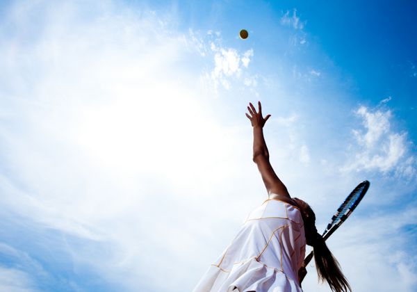 زن تنیس در لباس تنیس سفید که در حال توسعه سرویس توپ است