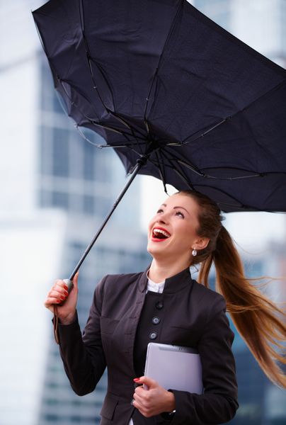 زن جوان كسب و كار با چتر در دست با وزش باد شديد كه در خارج از منزل مي جنگد