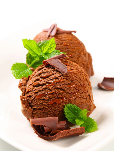 دو قاشق بستنی شکلاتی که با برگ نعنا و فرهای شکلاتی تزئین شده است