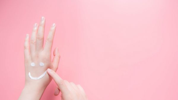 دستهای زن زیبا که از کرم مرطوب کننده در پس زمینه صورتی استفاده می کنند شکل خندان ایجاد شده از لوسیون مراقب پوست بدن خود باشید مفهوم مراقبت های بهداشتی و زیبایی نمای بالا فضا را کپی کنید