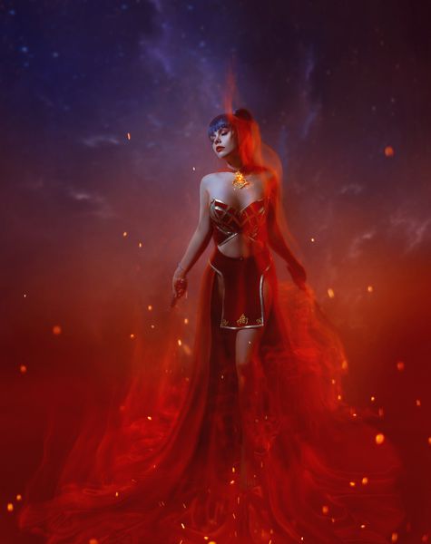 یک رزمنده آتش در یک شعله ایستاده یک دختر جوان لاغر زرق و برق دار با موهای بلند آبی لباس پوشیده از دامن شرقی و بالای قرمز شکم باز و شانه با گردنبند با سنگ آتشین تزئین شده است