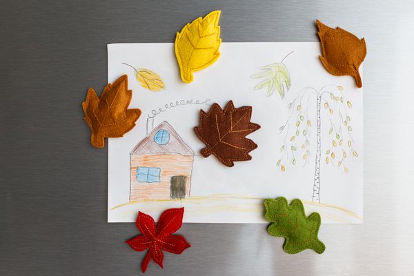 برگهای احساس رنگارنگ پاییزی روی درب یخچال و فریزر عکس کودکان با خانه و درختی که از درب یخچال آویزان شده اند آشپزخانه سفید روی زمینه دیه دکوراسیون پاییز پاییز برای خانه