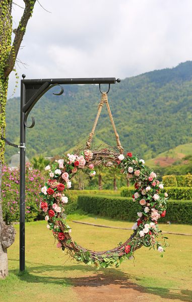 چرخش سبد عروسی زیبا با گلهای رزهای رنگارنگ تزئین شده در باغ طبیعت که به قطب زیر شاخه های درخت آویزان شده است