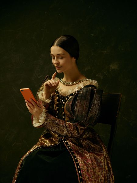 پرتره دختری که لباس شاهزاده خانم یا کنتراست را با تلفن همراه از طریق استودیوی تاریک در حال تهیه عکس سلفی می کند