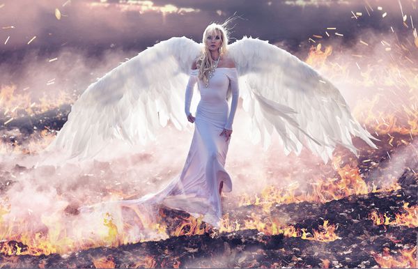 تصویر هنری زیبا زن فرشته ای خیره کننده که زمینه های آتش را در حال قدم زدن است