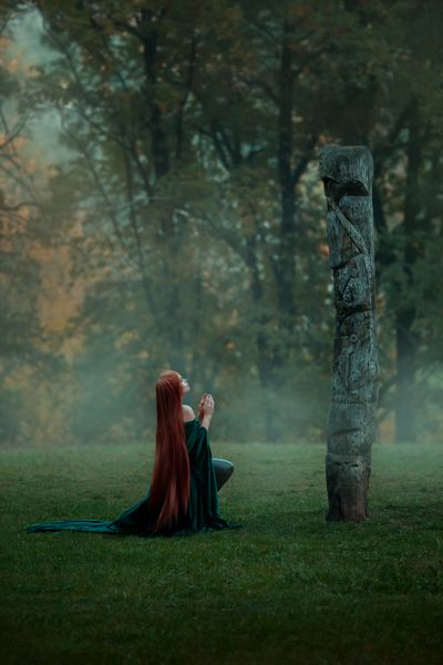دختر جوان womderful Merida در یک جنگل مه آلود زندگی می کند به پاکسازی در یک تپه می رود تا یک خدایان را برای نماز بخواند یک جادوگر سرخ در لباس مخملی بلند و زمستانی زمرد دلیرزاده زانو می زند بت چوبی