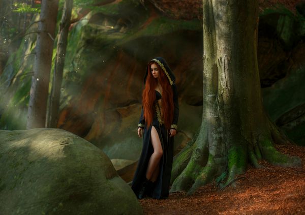جادوگری با موهای قرمز در یک لباس زمرد تیره و طولانی لباس خزدار چکمه های چرمی در جنگل در پرتوهای مهتاب کشیش آماده فداکاری مراسم عکس هنری با رنگهای خلاقانه گرم