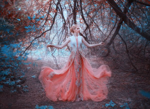 وروجک ملکه دلپذیر ایستاده در جنگل در نزدیکی شاخه های درختانی که زمین را لمس می کنند پوشیدن یک لباس تیز و زیبا صورتی هلو شگفت انگیز آن را به زمین می اندازد پرواز می کند پرواز