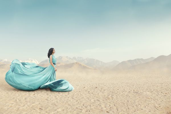 پرتره زن جوان زیبا با لباس طلسم بلند که در فضای باز در صحرای شنی قرار دارد