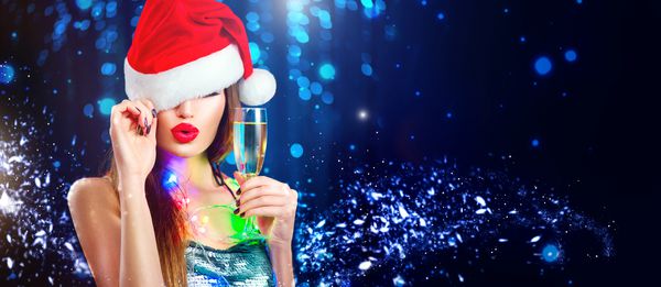 زن کریسمس دختر مدل زیبایی در کلاه بابا نوئل با لب قرمز لیوان شامپاین در دست خود جشن در مهمانی شبانه پرتره زرق و برق نزدیک در زمینه زمستانی گسترده با copyspace