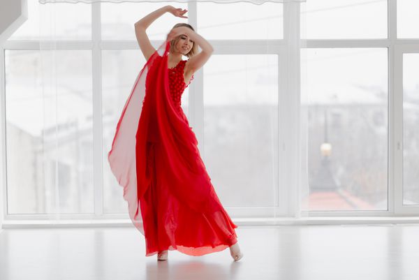 دختری به رنگ قرمز در اتاقی با پنجره های بزرگ در حال رقصیدن است