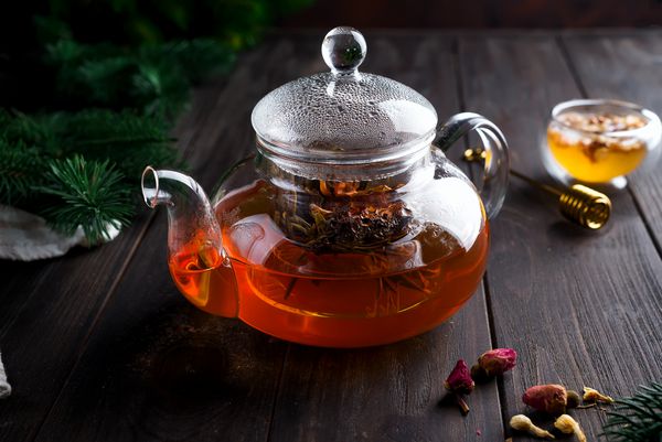 قوری شیشه ای با چای گیاهی تازه و عسل در یک زمینه چوبی کریسمس یا نوشیدنی زمستانی برای گرم کردن