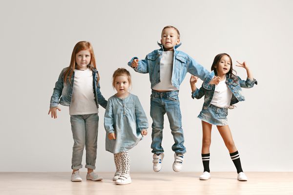 پرتره پسران و دختران بچه های ناز با لباس شلوار جین شیک که به دوربین مقابل دیوار استودیوی سفید نگاه می کنند کودکان و نوجوانان و مفهوم احساسات شاد