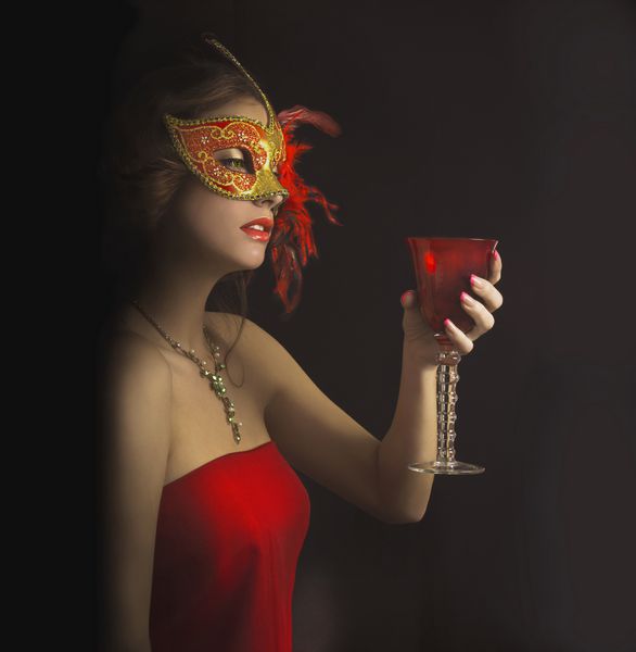 زن جوان زیبا در ماسک ونیزی مرموز قرمز با لیوان قرمز