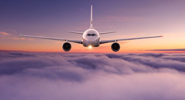 هواپیمای جت هواپیما تجاری که بر فراز ابرهای دراماتیک در نور غروب خورشید زیبا پرواز می کند مفهوم سفر