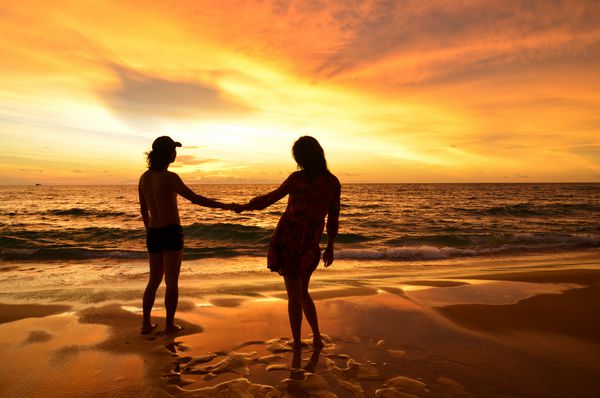 زن و شوهر جوانی که عاشق همدیگر هستند هنگام غروب آفتاب در ساحل کارون پوکت تایلند ابرهای سوزان را تماشا می کنند