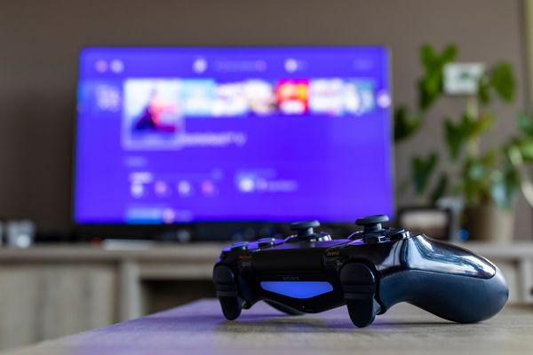 BRECHT BELGIUM 28 مارس 2019؛ یک پرتره از یک کنترلر PS4 که روشن است مقابل یک تلویزیون تلویزیون مبهم است و صفحه اصلی Playstation را به نمایش می گذارد