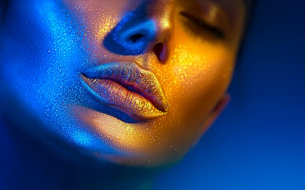 مدل صورت زنانه در جرقه های روشن چراغ های نئون رنگی لبهای زیبا دخترانه دهان آرایش پوست طلایی درخشان مرسوم مد روز طراحی هنری را تشکیل می دهد آرایش آبی طلایی براق فلزی