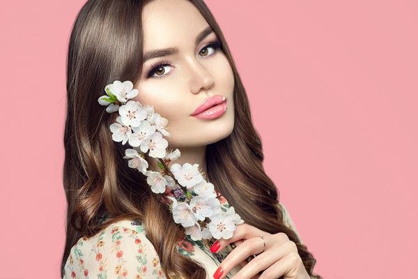 دختر تازه و زیبا با دسته گل شکوفه گل بهار ساکورا زن جوان و زیبایی با پوست جوان و آرایش کامل مدل کننده با گلهای تابستانی